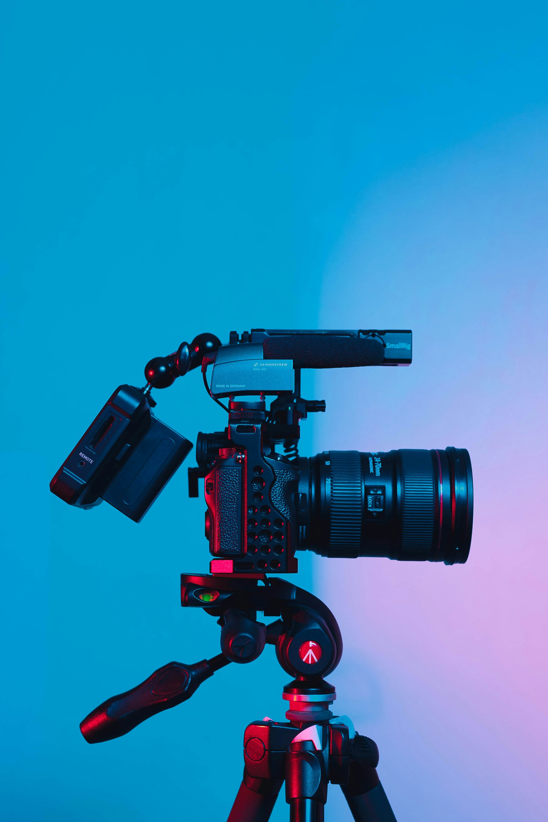 A video camera with a microphone mounted on a tripod against a soft blue and pink backdrop