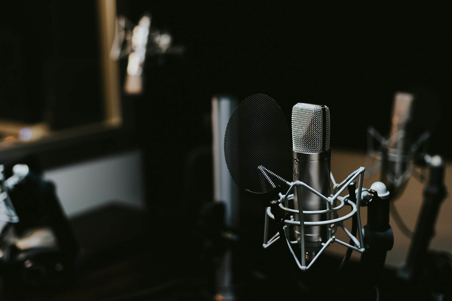 A studio condenser microphone in a shock mount, lit softly in the dark